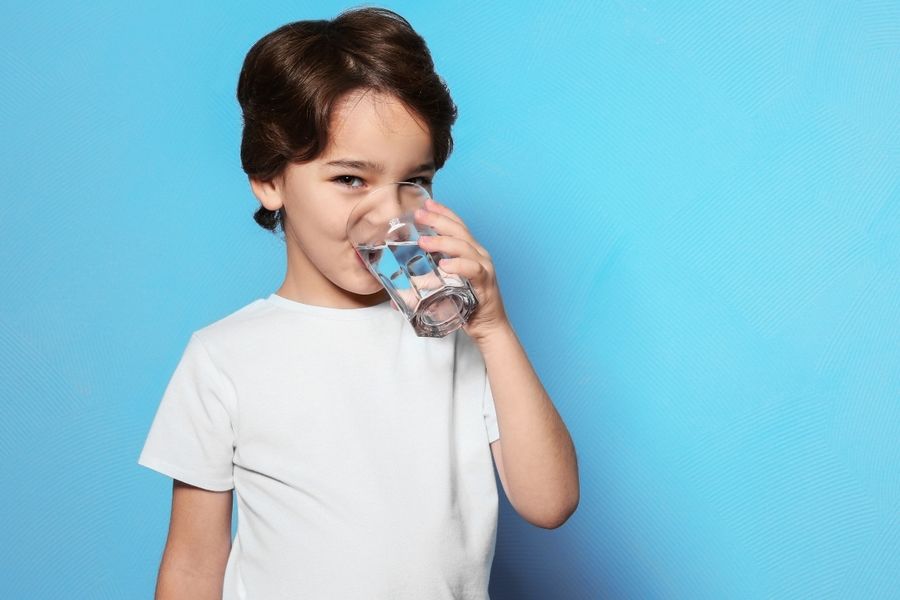 Image of a boy in a white t-shirt drinking a glass of water. Source: canva