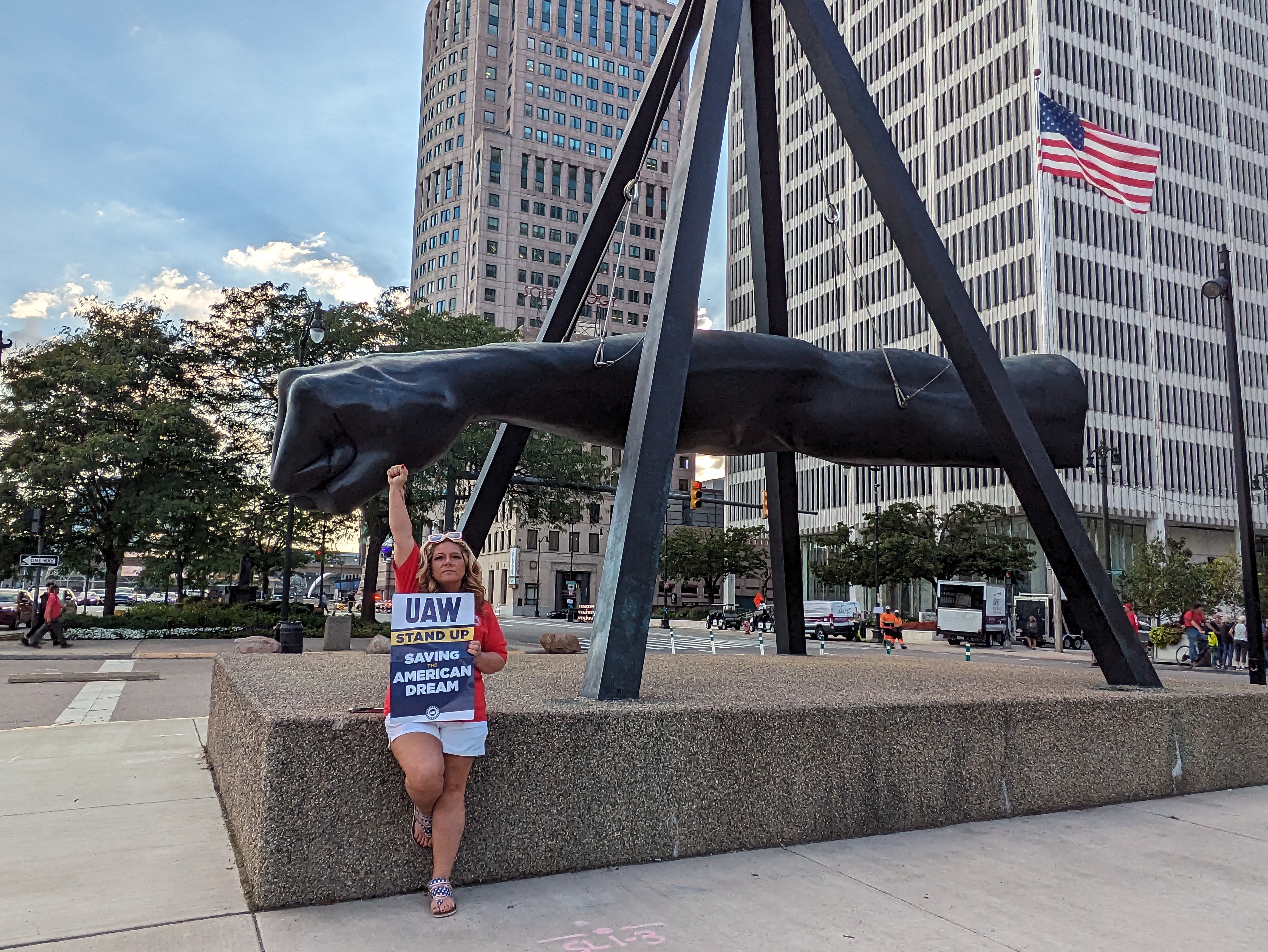 Joe Lewis fist statue in Detroit with UAW member holding her own fist up holding sign saying UAW Saving The American Dream