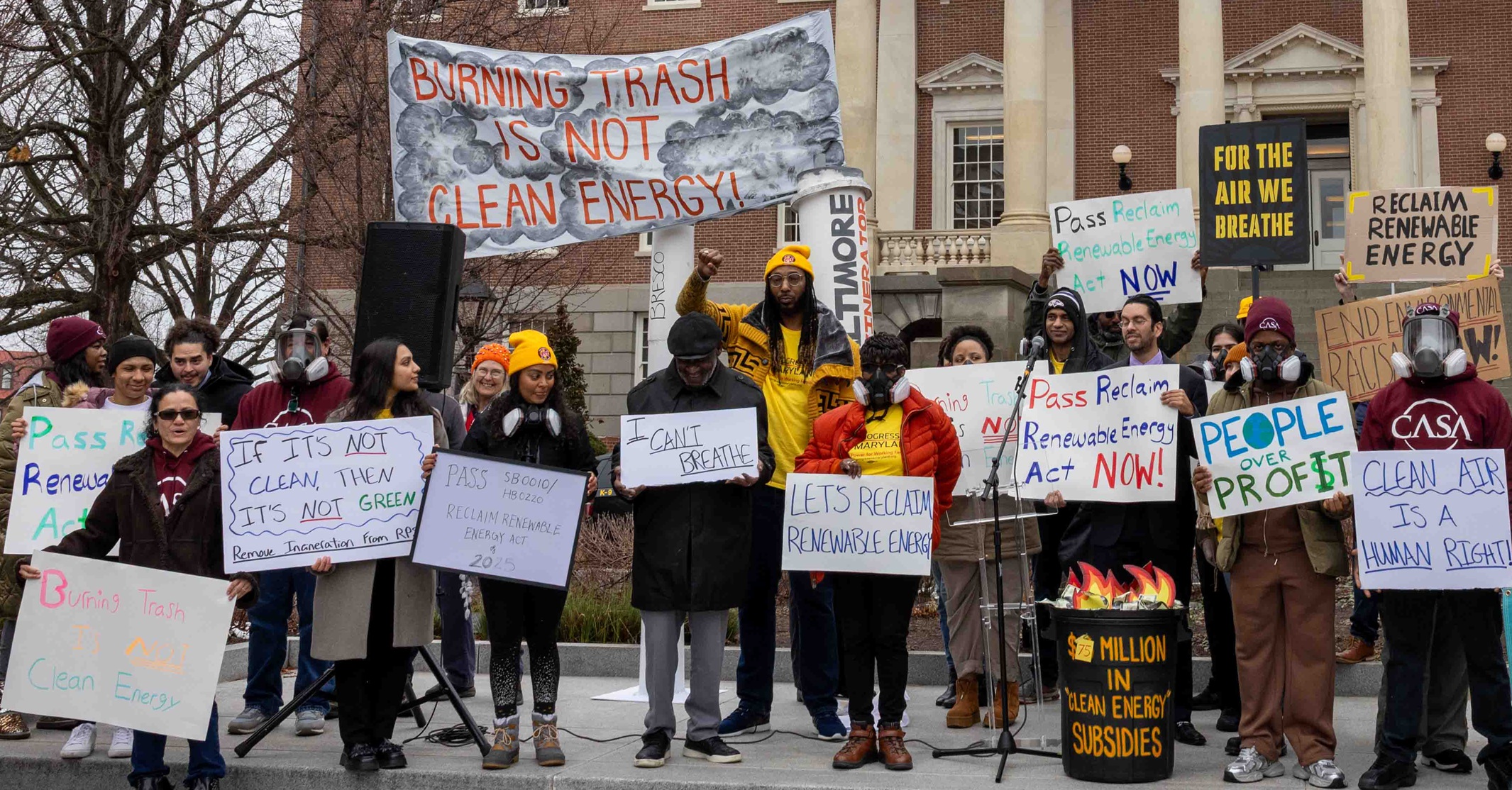 Picture of people protesting in Annapolis holding signs like "Burning trash is not clean energy," "For the air we breathe," "Let's Reclaim Renewable Energy."