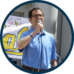 Igor Tregub speaking into a microphone in front of a rally