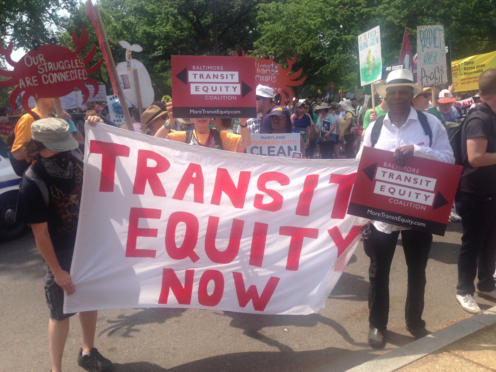 Supporters of the Baltimore Transit Equity Coalition hold a sign that reads "Transit Equity Now"