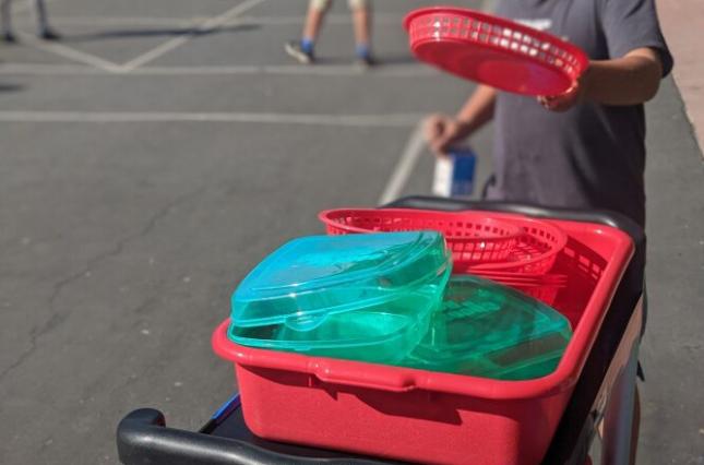 Child putting reusable basket into bin next to sign with cheerful silverware graphic saying "We Go Here!"