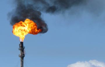 Gas flare fire and black smoke on blue sky day. 