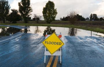 Image: A flooded road with a sign that says Flooded. Source: Canva