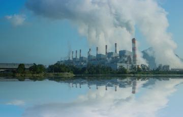 Image of a coal fired power plant by a body of water. Canva image.