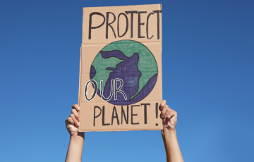 cardboard sign that reads protect our planet with a planet drawn in middle