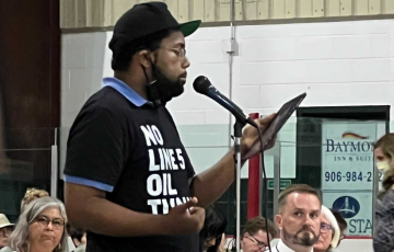 Erik McCleary testifying at USACE hearing wearing No Line 5 Oil Tunnel shirt.