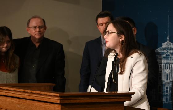 Amara Strande speaking at podium with her father and mother at the side
