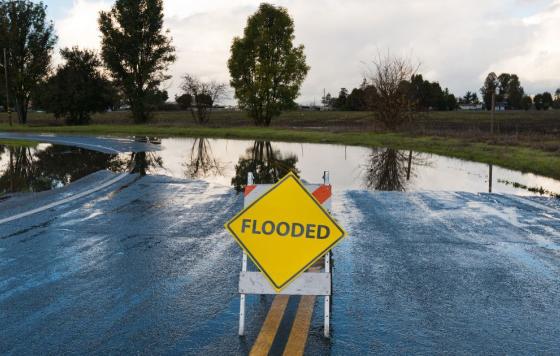 Image: A flooded road with a sign that says Flooded. Source: Canva