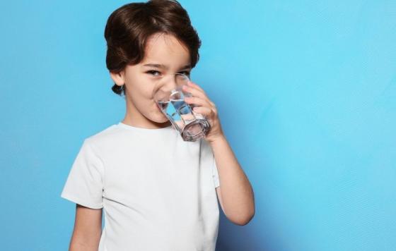 Image of a boy in a white t-shirt drinking a glass of water. Source: canva