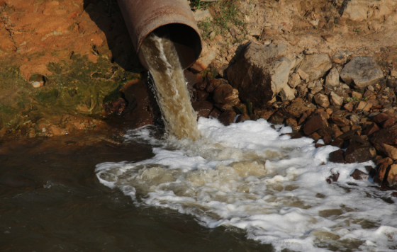 Corroded pipe sprewing direty water into a stream