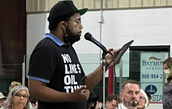 Erik McCleary testifying at USACE hearing wearing No Line 5 Oil Tunnel shirt.